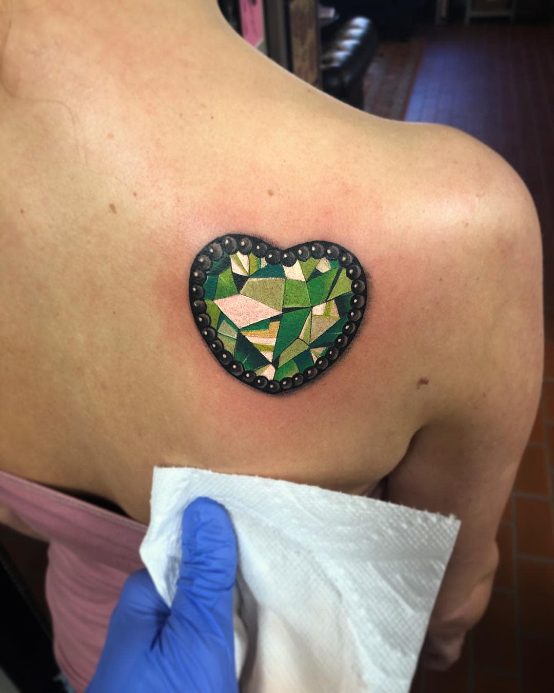A tattoo of emerald heart on the upper back on the right shoulder