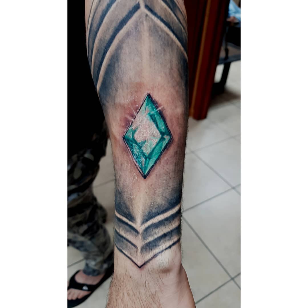 Tattoo of a green and blue 3D gemstone with geometric designs on a forearm