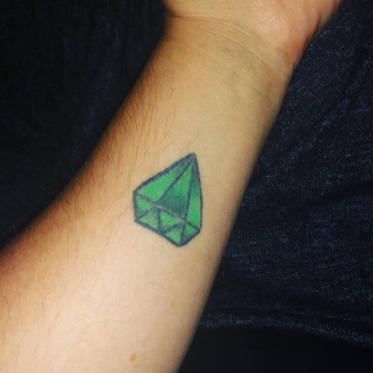 A wrist tattoo featuring an emerald