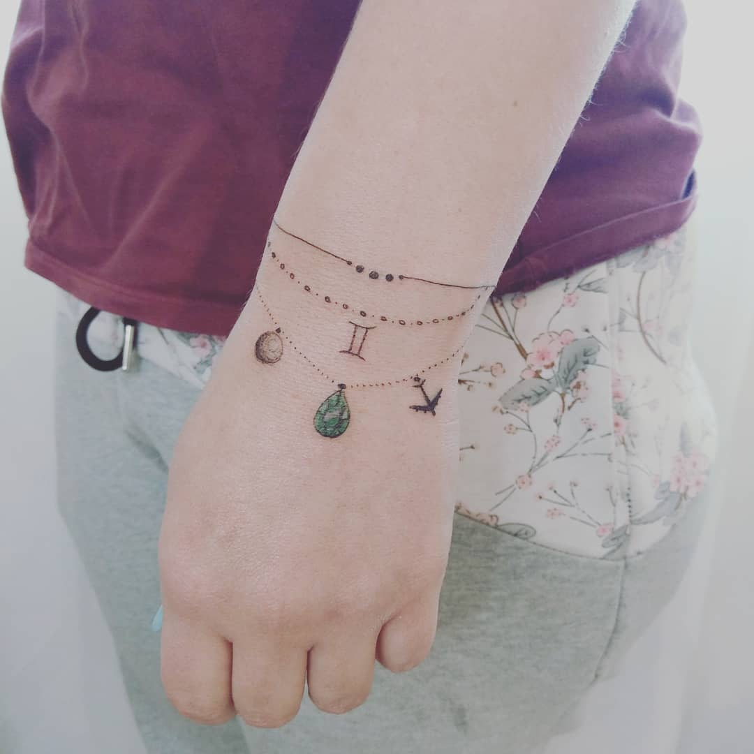 Delicate celestial tattoos on wrist with emerald stone