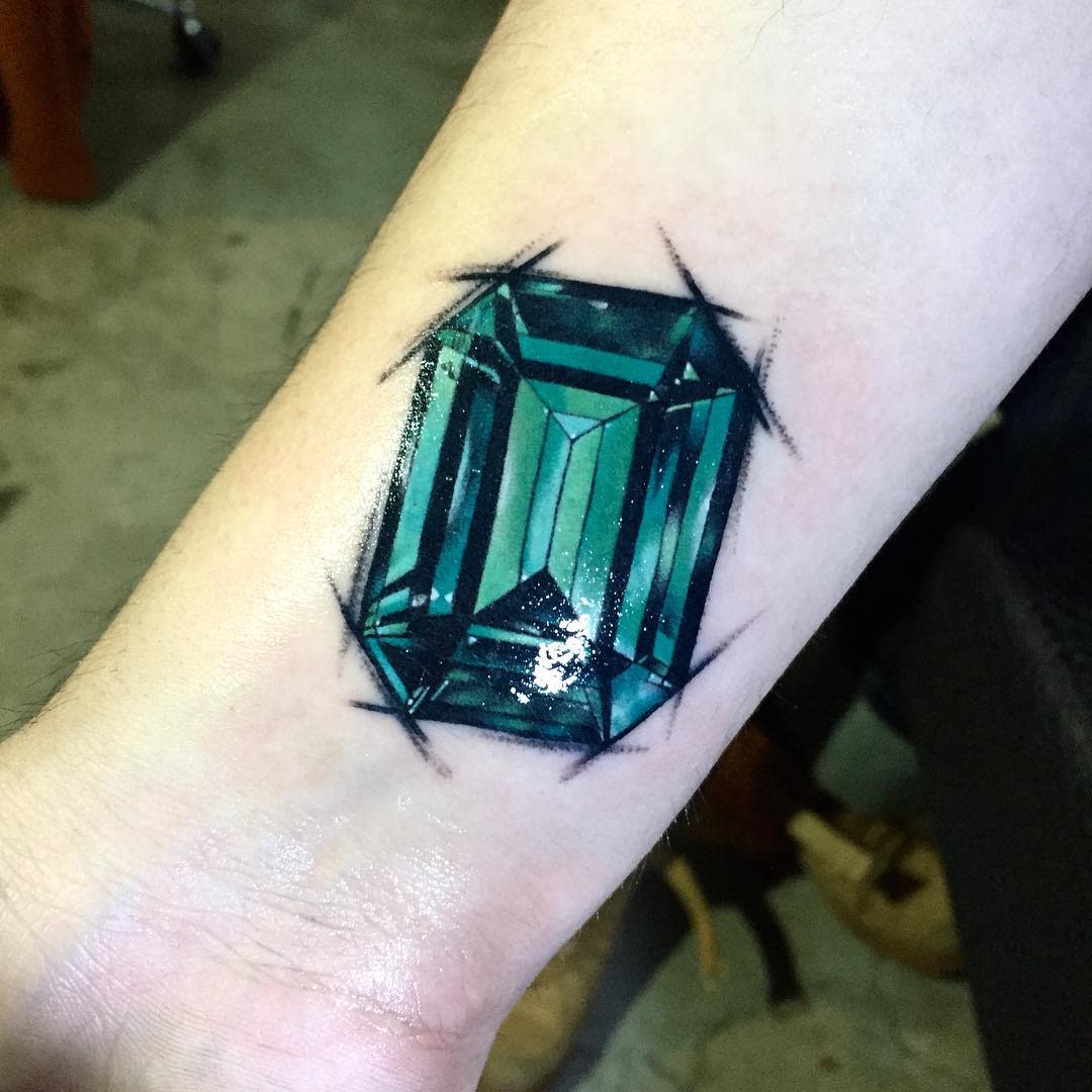 A detailed tattoo of an emerald gemstone on a forearm