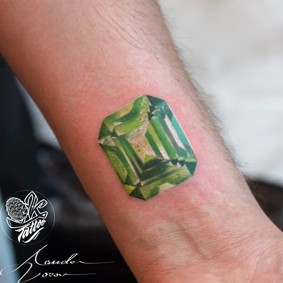 Tattoo of a green, emerald-cut gemstone on a forearm