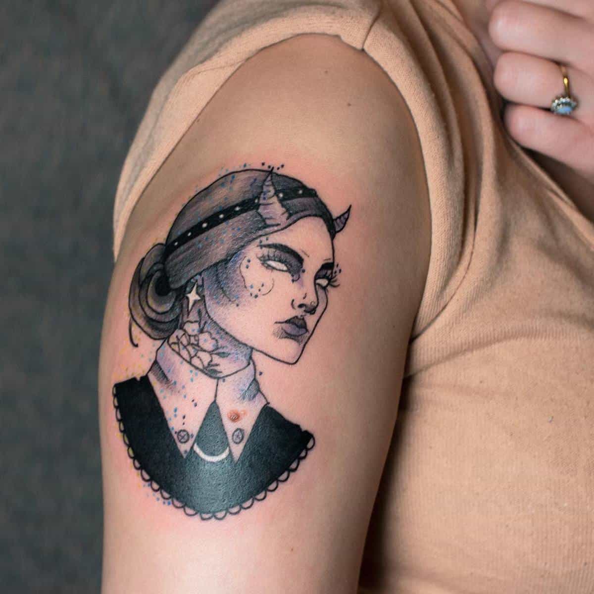 Tattoo of a woman's face with devil horns on someone's upper arm