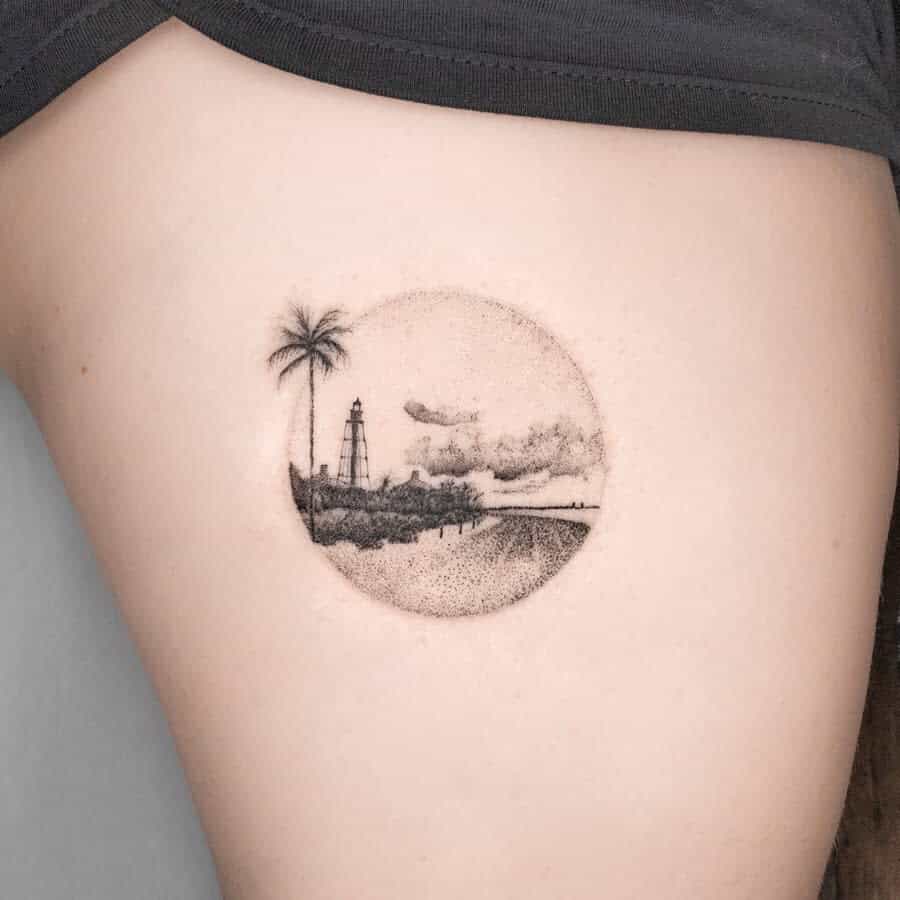 Tattoo of a beach scene with a palm tree, lighthouse, and cloudy sky delicately rendered in single needle technique on someone's skin