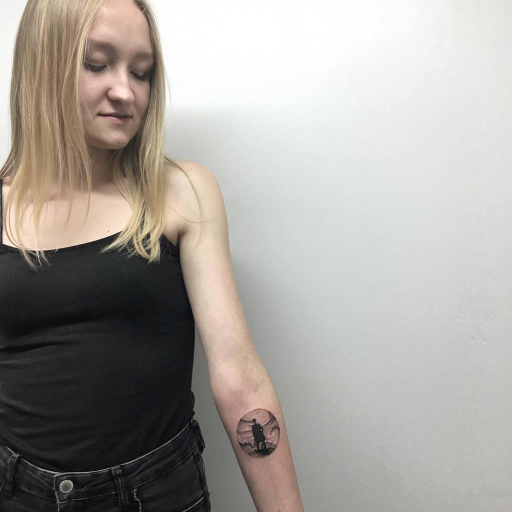 Person with long blonde hair showing off a single needle circular tattoo on their forearm