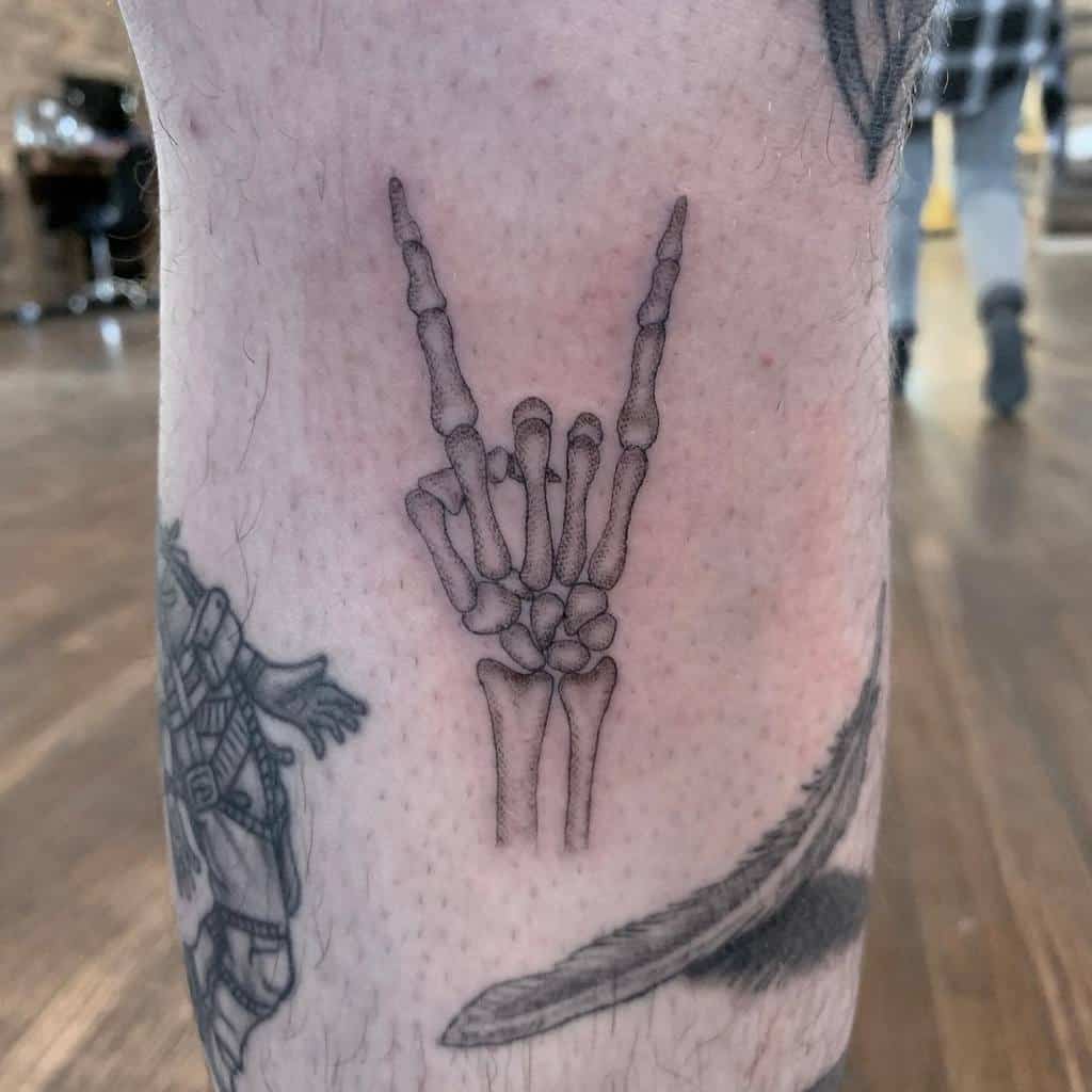 Tattoo of a skeletal hand making a rock 'n' roll gesture on a person's leg skillfully crafted with single needle precision
