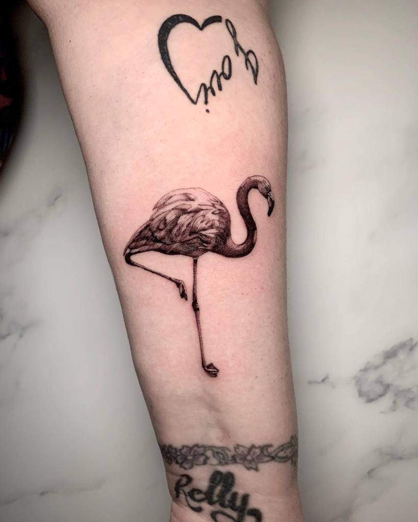 Arm with single needle flamingo tattoo and heart tattoo above it on light background