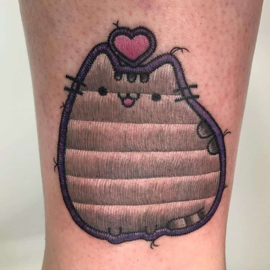 Patch-style tattoo of a plump tabby cat with a purple outline, detailed stitched textures, and a floating heart above its head.