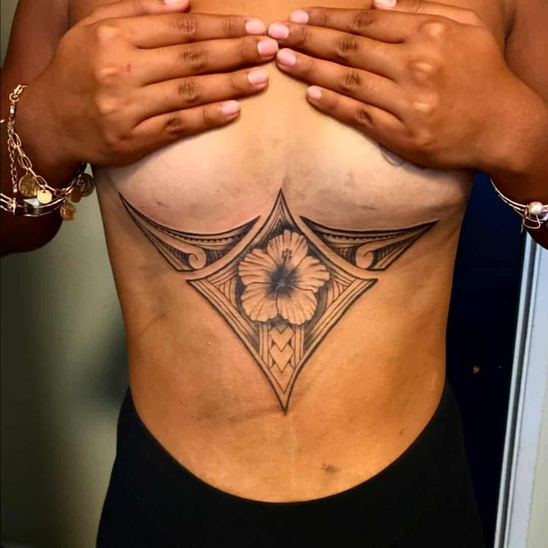 Hands covering chest, revealing a large geometric and floral tattoo design on the upper abdomen area inspired by Polynesian artistry
