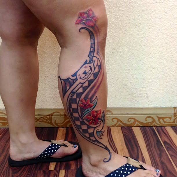 Tattoo of a Polynesian-inspired checkered flower design with red flowers on the back of a leg, wearing polka dot sandals