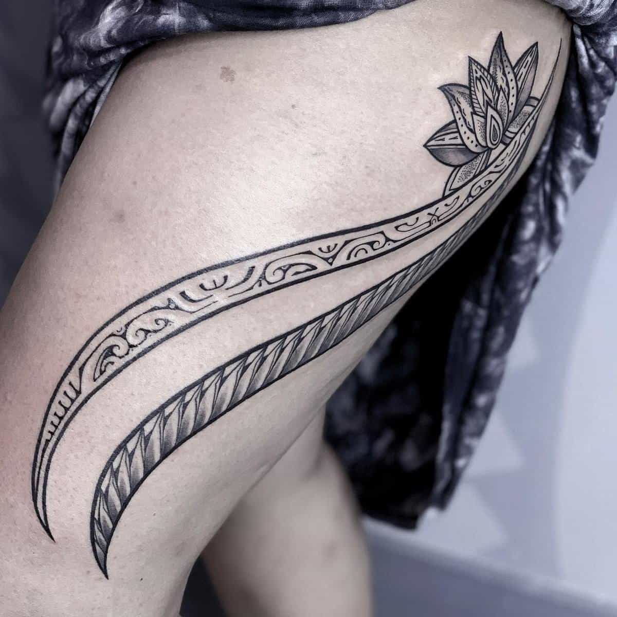 Tattoo of a detailed lotus flower intertwined with long, curved Polynesian tribal designs on a thigh