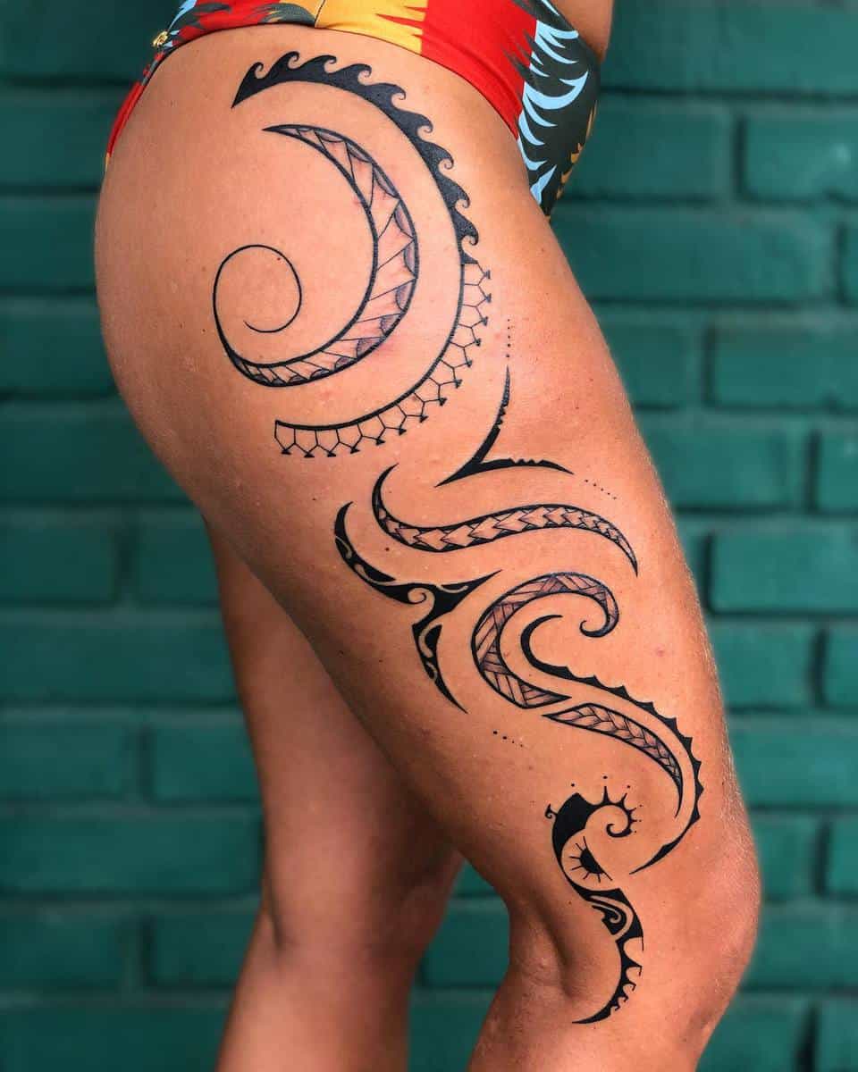 A thigh with ornate, curving black Polynesian tattoos, wearing a colorful swimsuit, against a green brick wall
