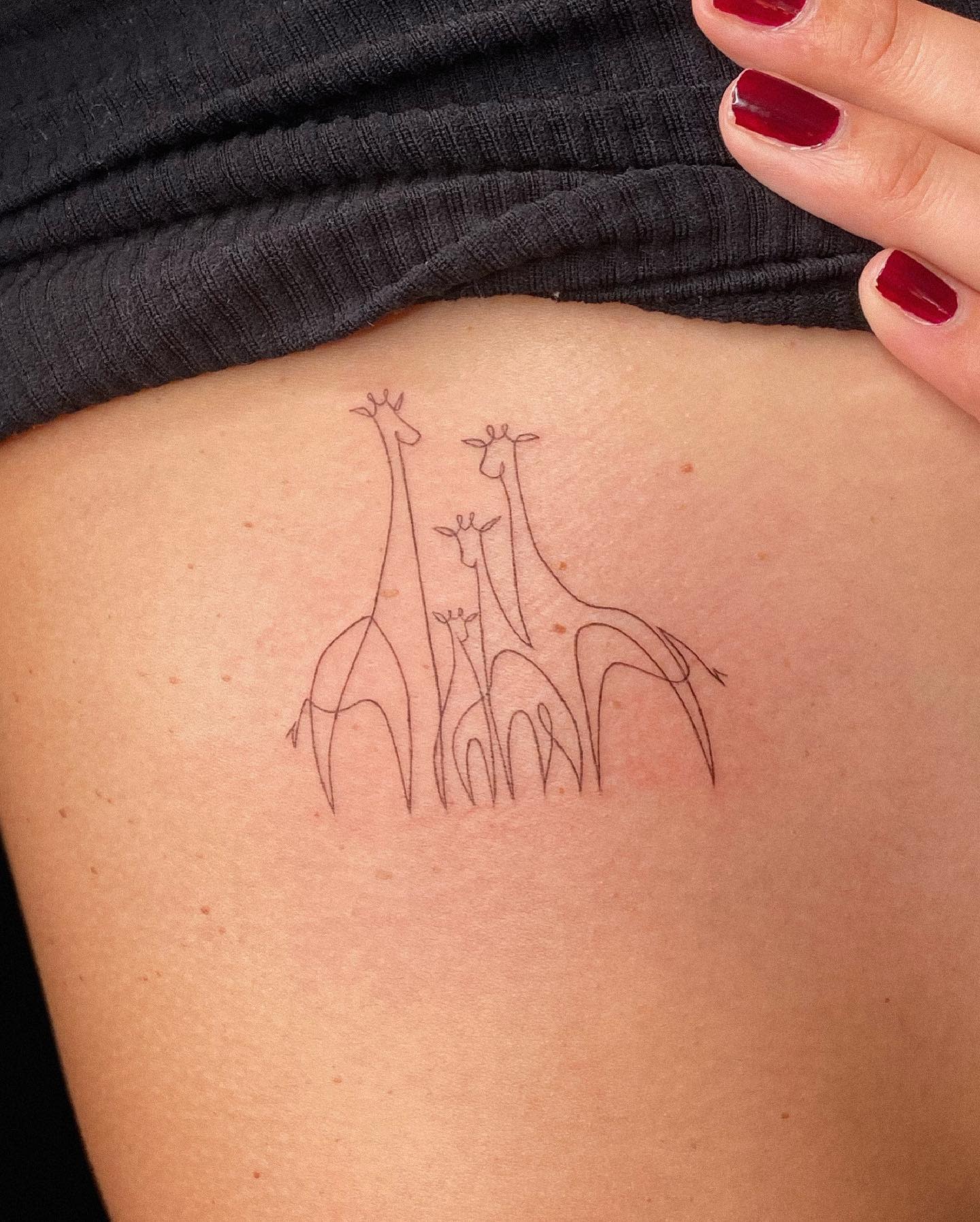 Minimalist tattoo of a family of five giraffes on skin