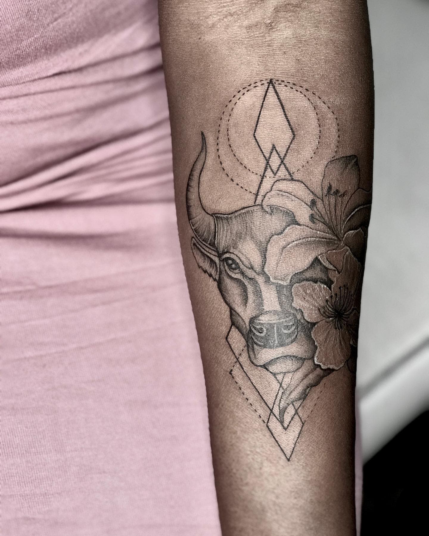 Bull with geometric shapes and floral elements tattooed on forearm