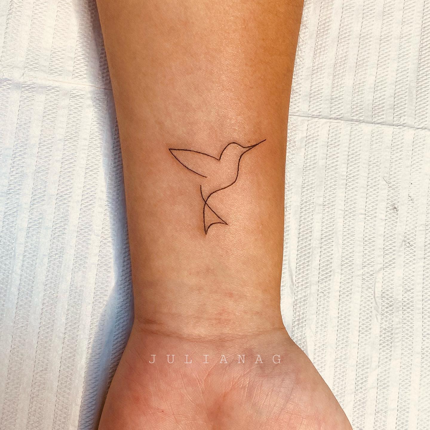 A minimalist hummingbird outlined tattoo on the inner forearm with no shading
