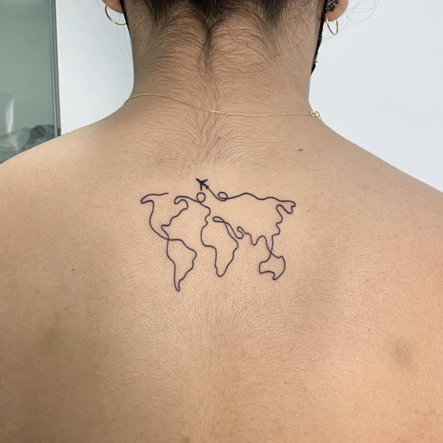 Line art tattoo of a world map with an arrow on the upper back