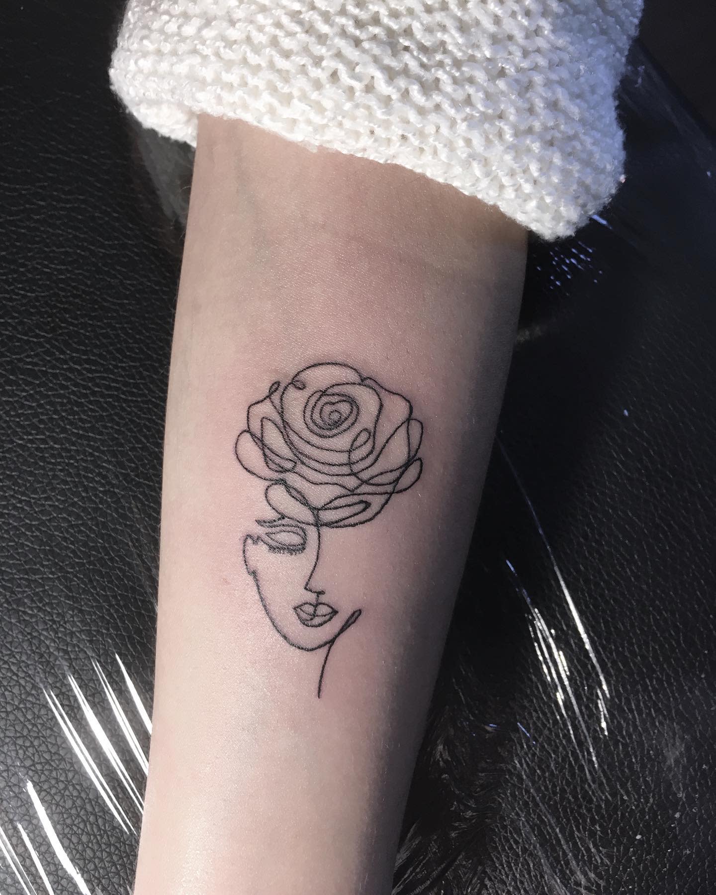 A woman's face merged with a rose bloom on inner forearm