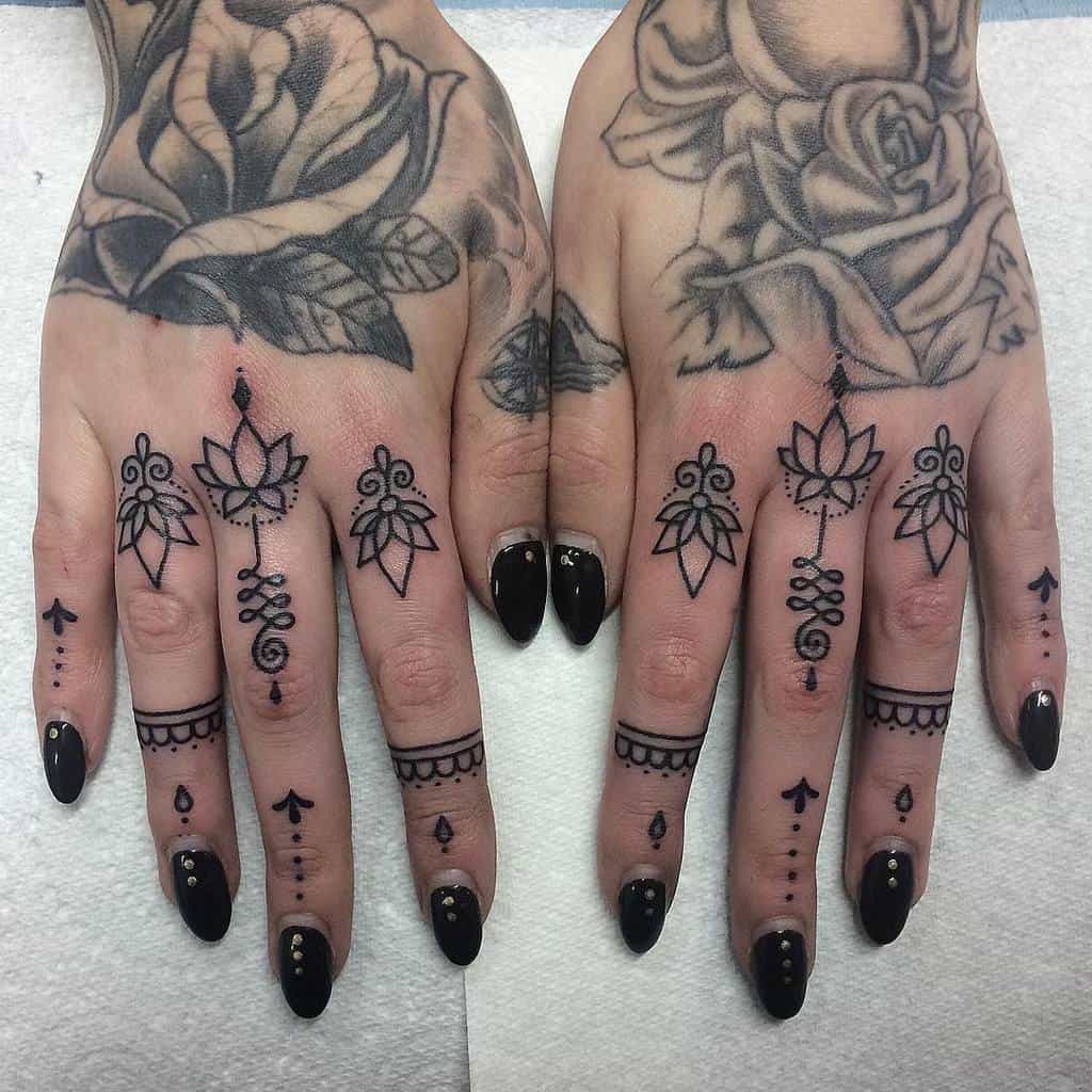 Ornamental finger tattoos featuring lotus flowers, geometric patterns, dots, and decorative accents, with large rose and leaves