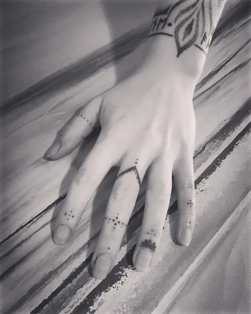 Minimalist finger tattoos featuring delicate dot patterns, geometric accents, and an ornamental wrist tattoo with intricate linework
