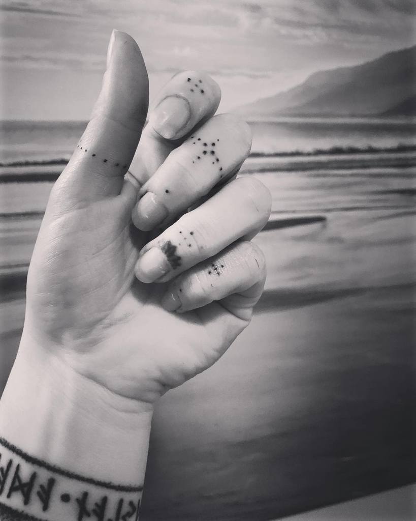 Minimalist finger tattoos featuring delicate dot patterns and geometric accents, paired with a bold wristband tattoo with runic symbols