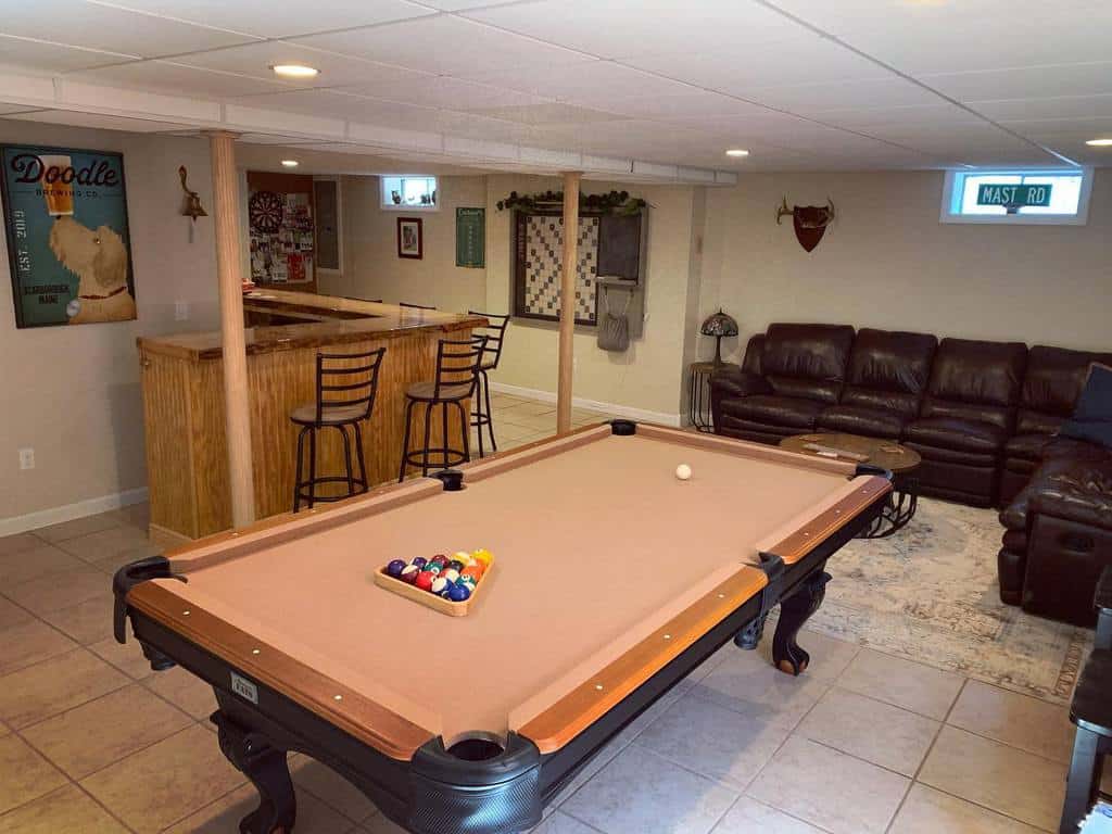 Basement with billiard table, wooden bar counter, and leather sectional seating.