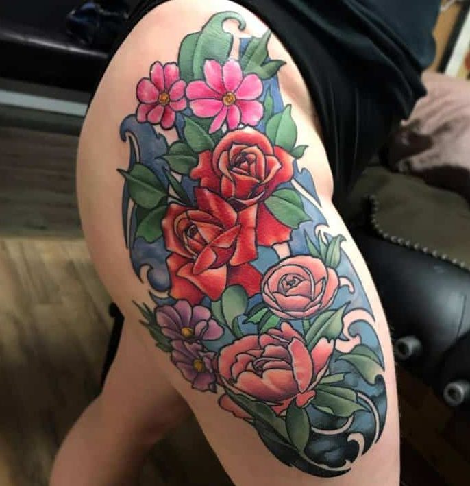 Art Nouveau thigh tattoo with red and pink roses, swirling blue accents, and lush green leaves in an elegant, flowing design
