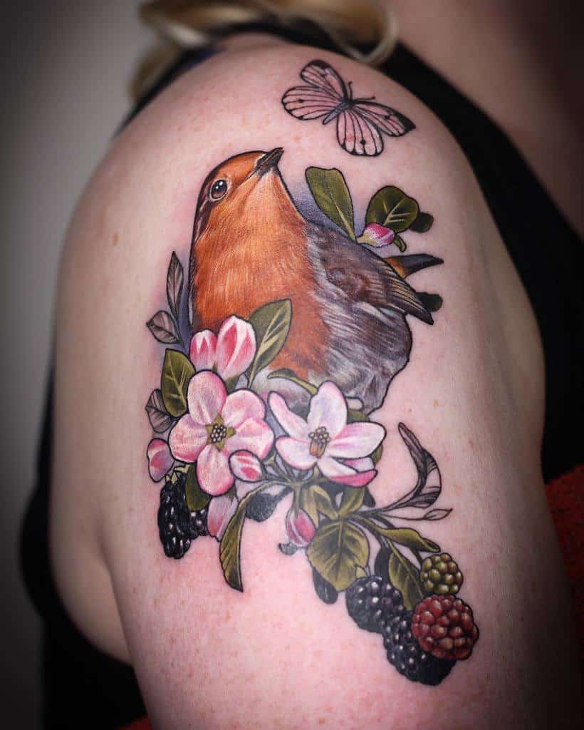 Colorful tattoo of a robin perched among pink blossoms, green leaves, and blackberries, with a pink butterfly above