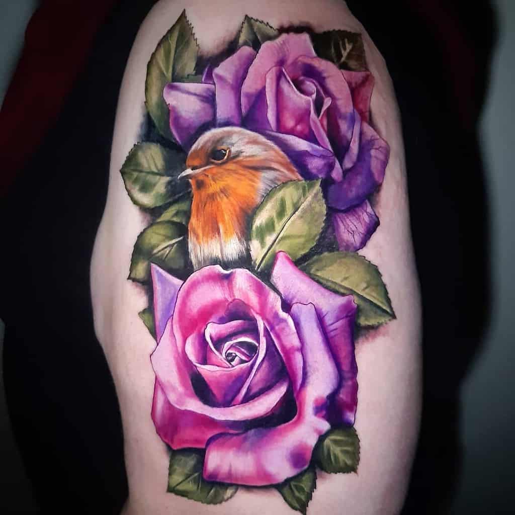 Colorful tattoo of a robin surrounded by vibrant purple roses and green leaves