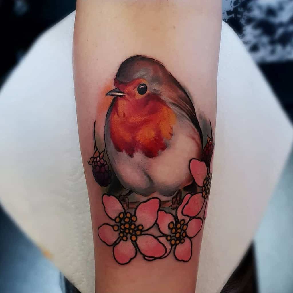 Colorful tattoo of a big robin perched on a branch with pink flowers and berries