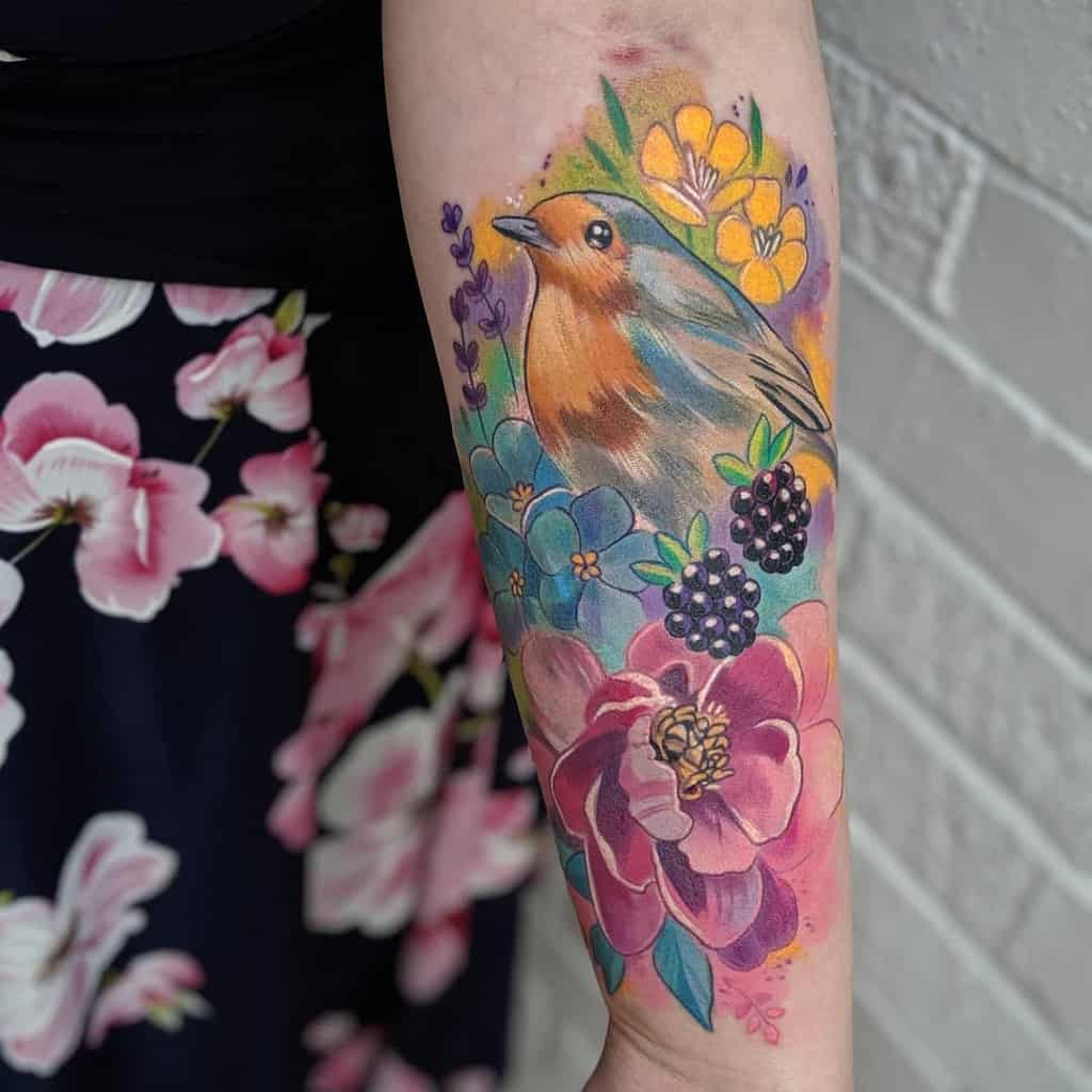 Colorful tattoo of a robin surrounded by vibrant flowers, blackberries, and leaves, featuring a watercolor-style background with soft shading