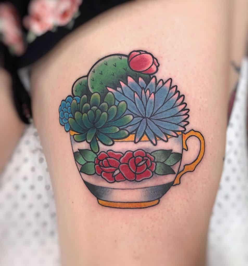 Colorful tattoo of a teacup filled with succulents and a blooming cactus, featuring vibrant floral patterns and a vintage design