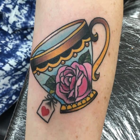 Colorful tattoo of a vintage teacup with a pink rose and a tea bag, featuring a heart on the tea bag's tag