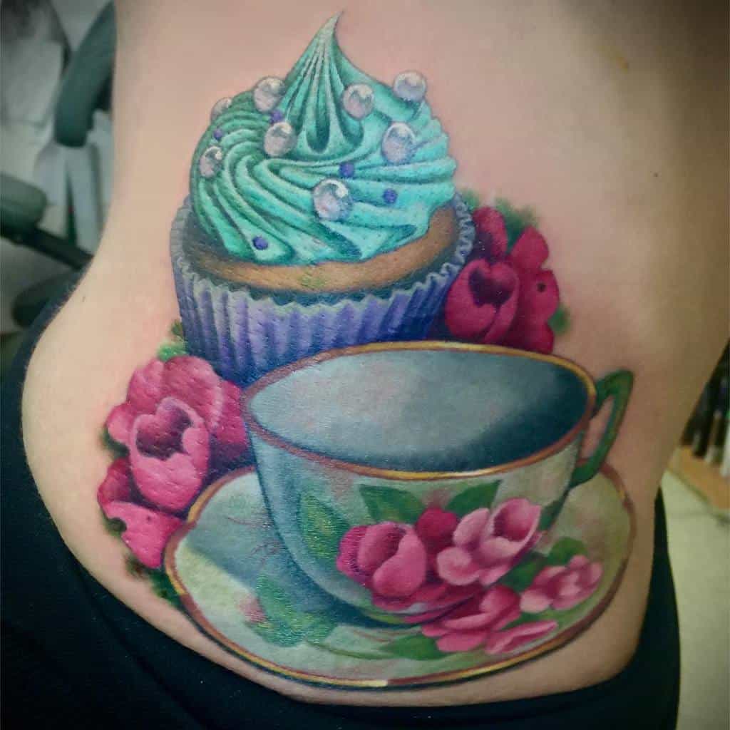 Colorful tattoo of a teacup with a saucer, pink flowers, and a frosted cupcake with pearls