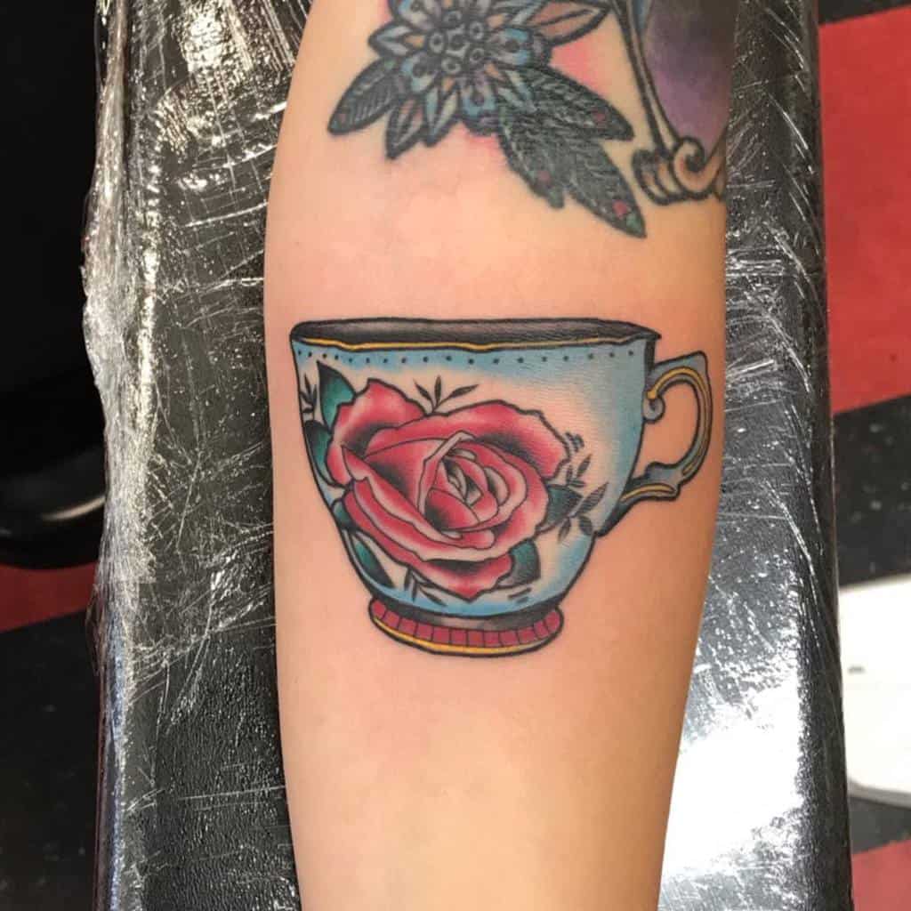 Colorful tattoo of a vintage teacup with a large red rose design, featuring bold outlines and a classic traditional style