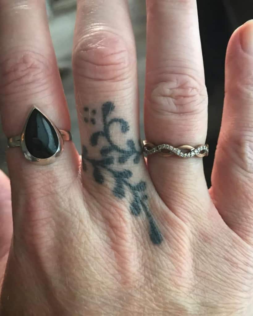 A detailed black ink ring tattoo featuring delicate floral patterns with swirls and small dots