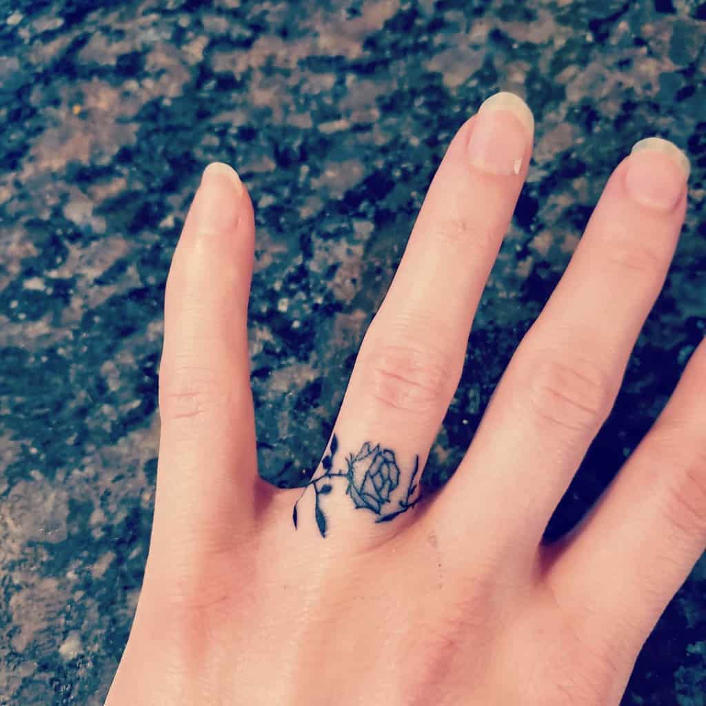 A beautiful and delicate ring tattoo featuring a small rose with leaves