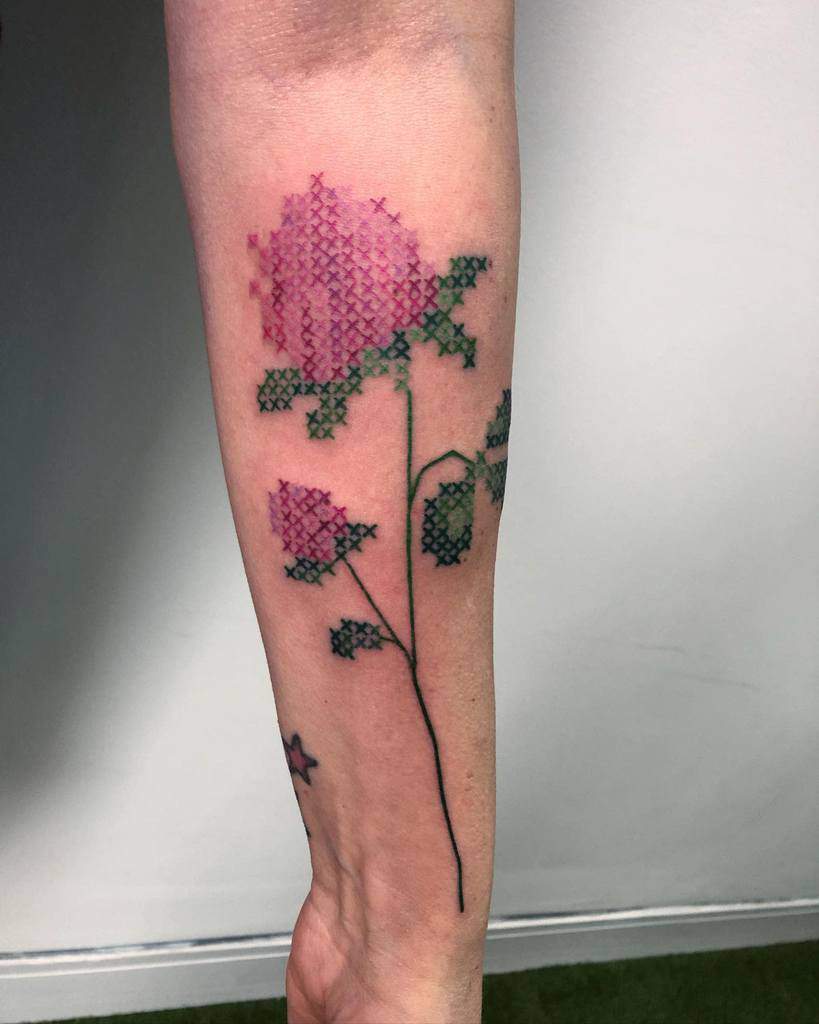 Cross-stitch tattoo of a pink and green floral design, resembling embroidered stitches for a unique, handmade effect