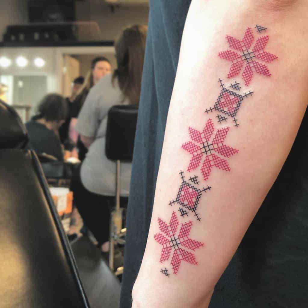 Cross-stitch tattoo with red geometric floral patterns, mimicking traditional embroidery for a unique folk-inspired design