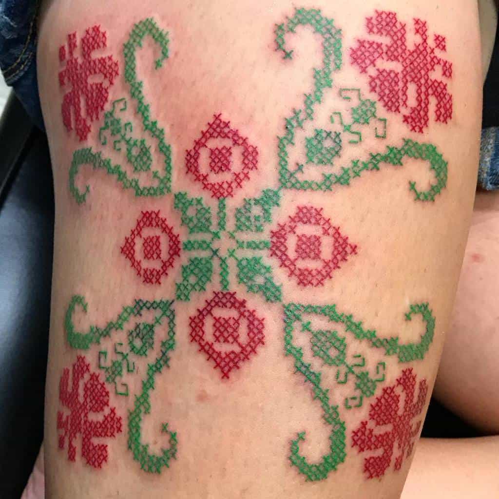 Cross-stitch tattoo with red and green symmetrical folk patterns, designed to mimic traditional embroidery