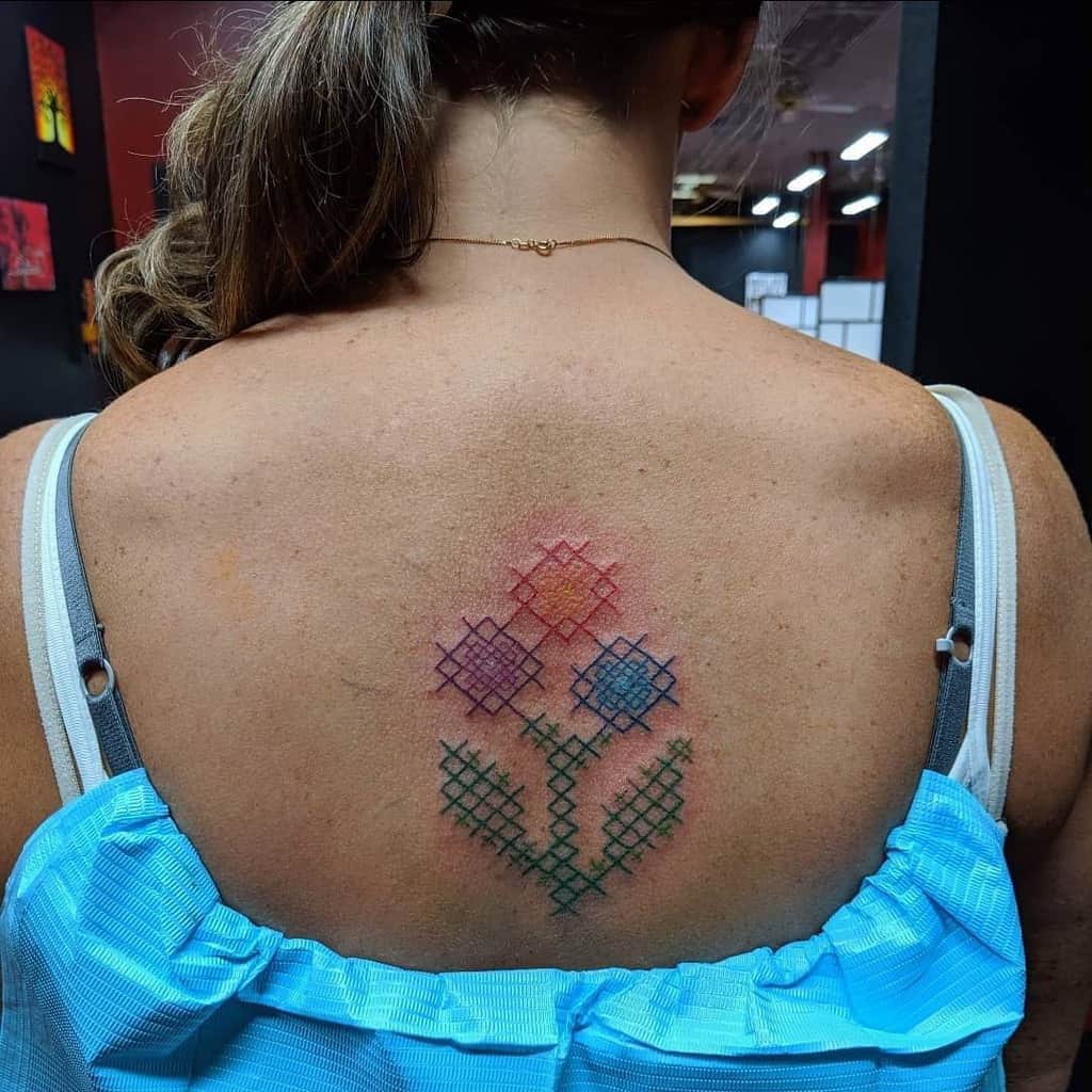 Cross-stitch tattoo of three colorful flowers, designed to resemble embroidery with a delicate and handmade aesthetic