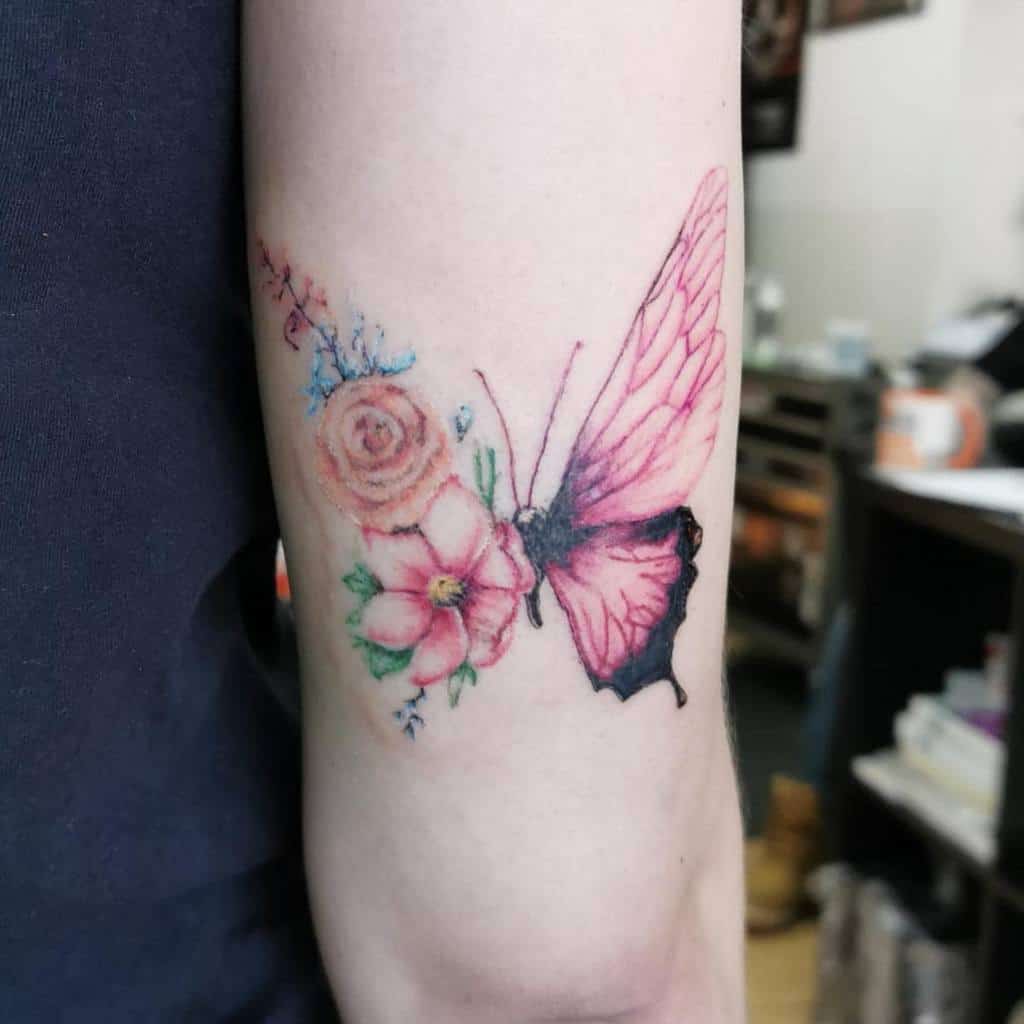 A delicate tattoo of a pink butterfly with floral accents on an arm