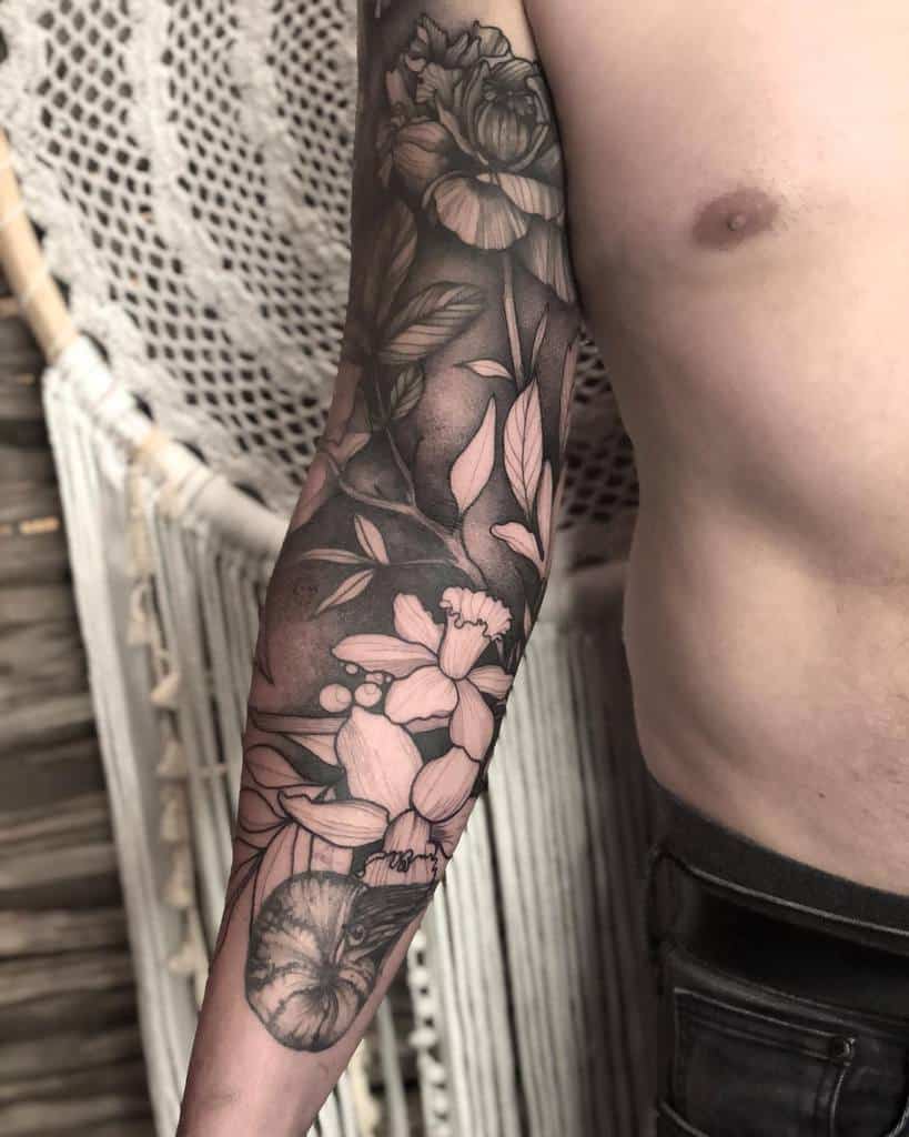 Black and gray floral sleeve tattoo with intricate blooms, leaves, and shading, blending soft and bold elements seamlessly