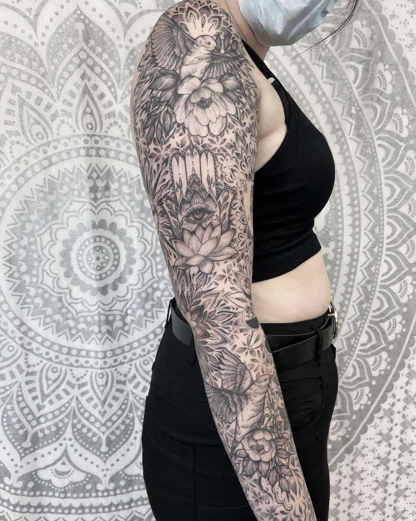 Stunning black and white sleeve tattoo featuring detailed floral motifs, a prominent all-seeing eye, a graceful dove, and intricate geometric patterns, creating a harmonious and symbolic design