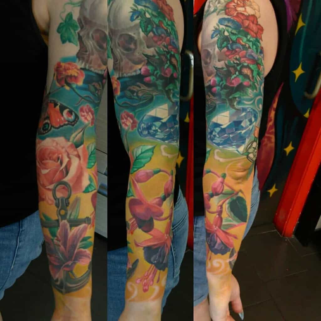 Vibrant full-sleeve tattoo featuring colorful roses, butterflies, a skull, and rich details, blending nature with artistic elements