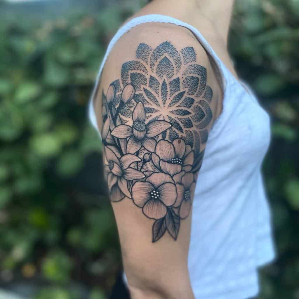 A detailed floral tattoo on a woman's upper arm, featuring intricate flowers and geometric patterns
