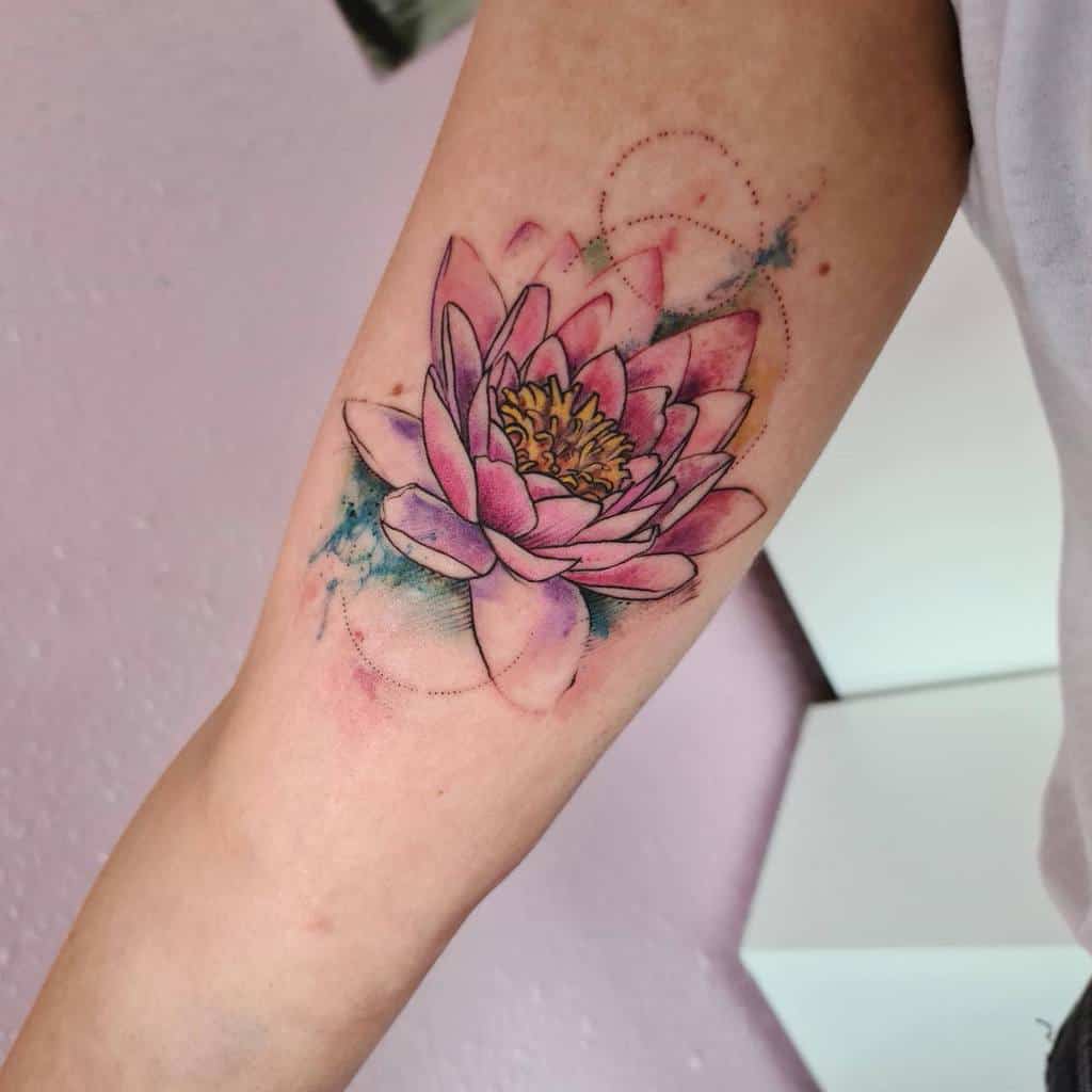 A vibrant pink lotus flower tattoo on an arm, with watercolor splashes in the background