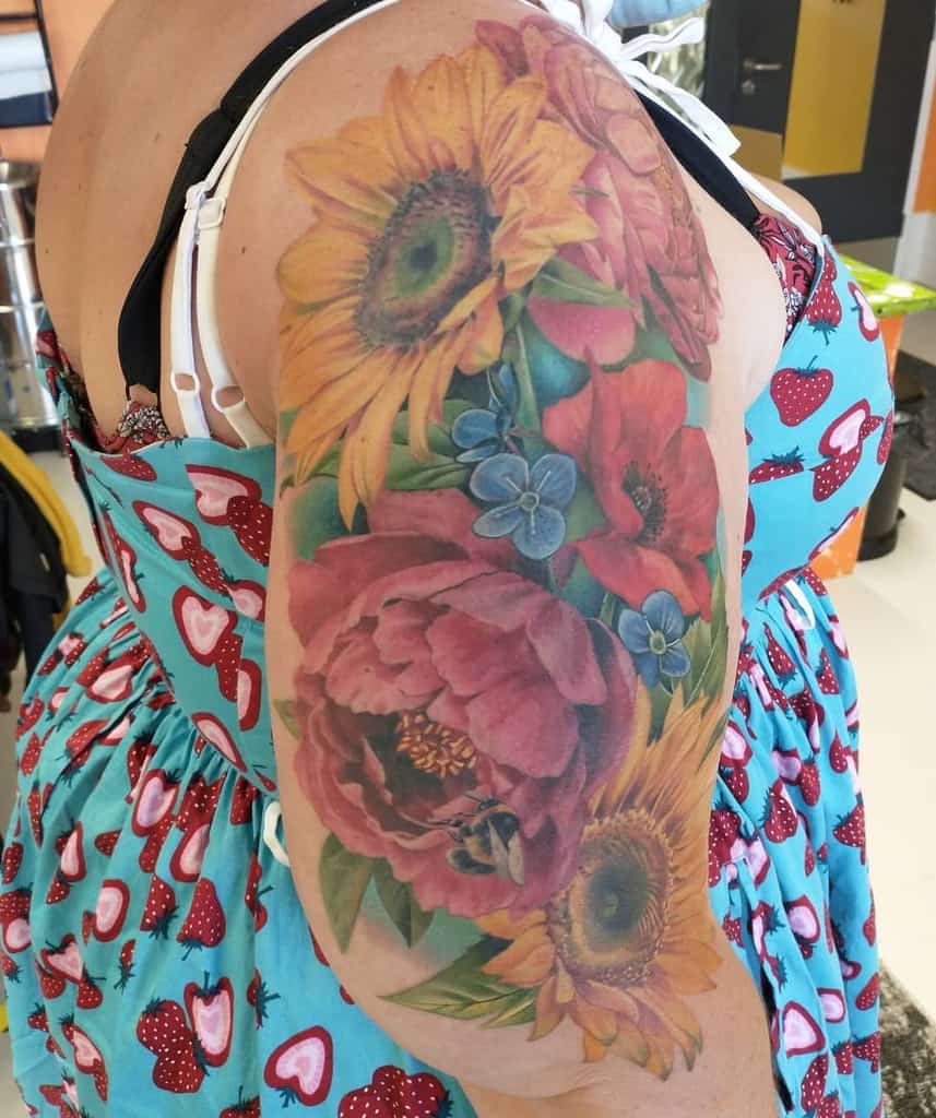 A colorful floral tattoo sleeve featuring sunflowers, roses, and other flowers on a woman's upper arm