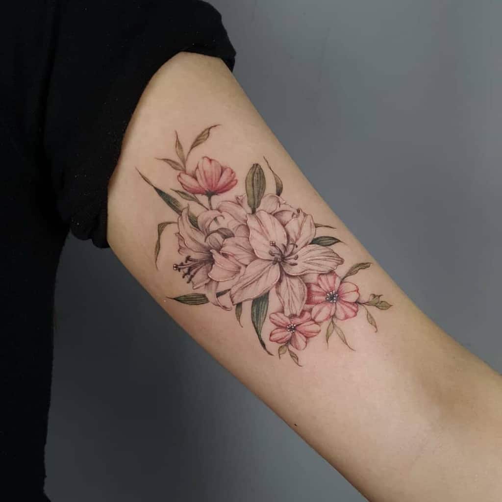 Floral tattoo on upper arm featuring pink and white lilies with green leaves