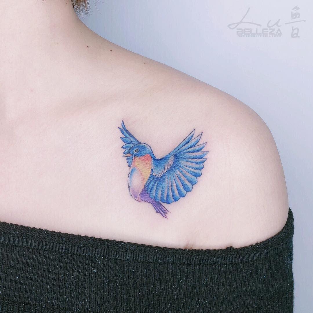 A colorful tattoo of a bird with outstretched wings on an upper shoulder
