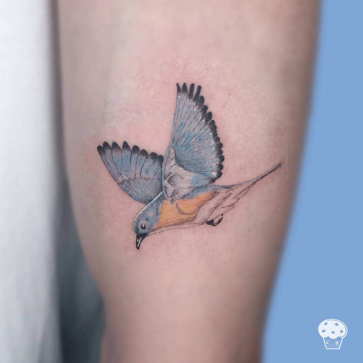 A tattoo of a flying bird with blue and orange feathers on skin
